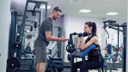 Beautiful athletic young woman making exercise at the gym. Exercises for biceps. Personal training.
