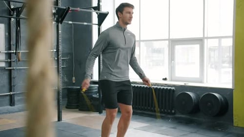 Hübscher Sportler, der drinnen im Fitnessstudio mit Seilspringen springt und sich auf Cardio-Training konzentriert