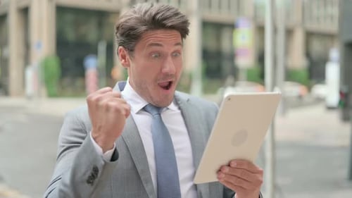 Man in Suit Celebrating with Tablet Outdoors
