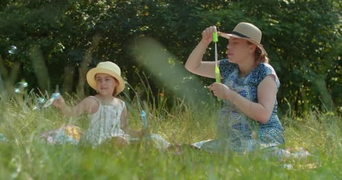 Mother and Preschool Daughter Blow Bubbles in the Park