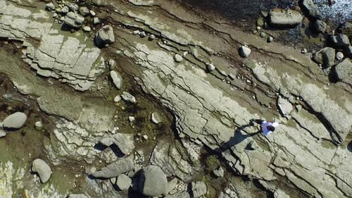 Aerial shot of young man running on a scenic rocky beach coastline.