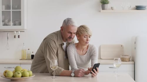 Concerned Couple Looking at Smartphone in Kitchen