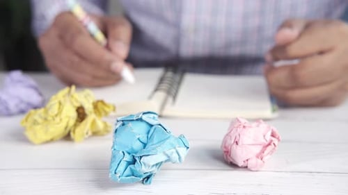 Crumpled Paper Ball and Man Writing on Notepad