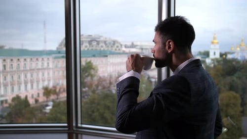 Businessman Drinking Coffee Overlooking City From Highrise