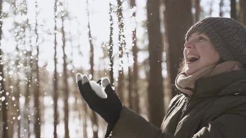 Happy Young Woman with Smile Throws Up Snow in Sunny Forest