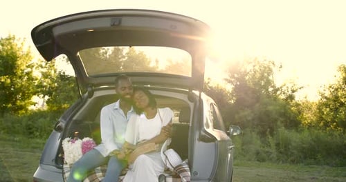 Romantic Young Adult Couple Sitting in SUV Trunk