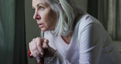 Senior Woman Resting Hands on Cane by Window
