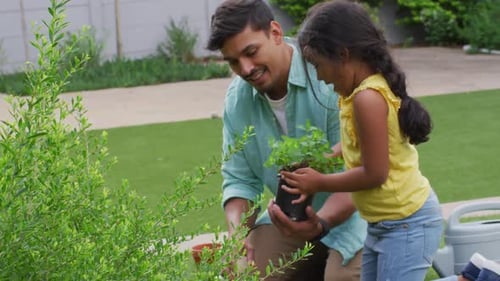 Hispanic father and daughter teaching planting flowers in the garden