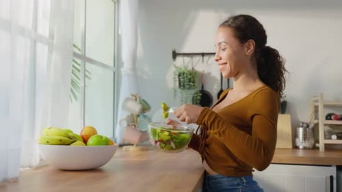 Latino attractive young woman eat green salad healthy foods for health care in kitchen at home.