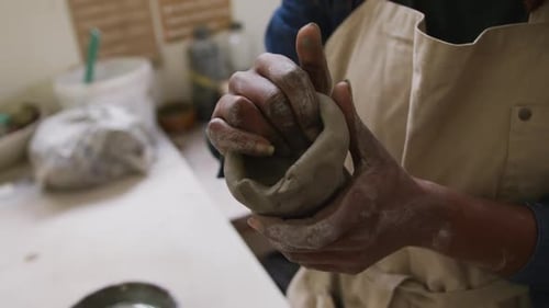Mid section of female potter wearing apron working on clay to create pot at pottery studio