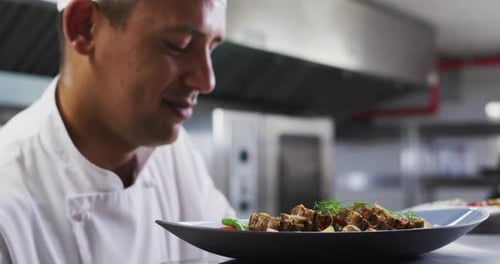 Caucasian male chef garnishing dish and smiling in restaurant kitchen