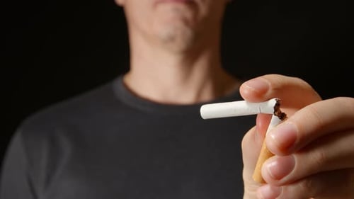 Jeune homme adulte tient une cigarette à une main puis la casse