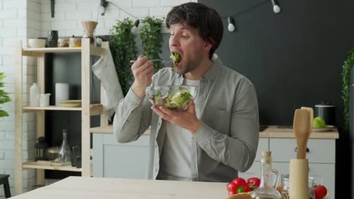 Man Eating Fresh Salad in Bright Kitchen