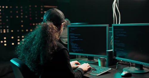 Concentrated and Anxious Hacker Wearing a Sweatshirt and Cap Breaking Into Corporate Data Servers