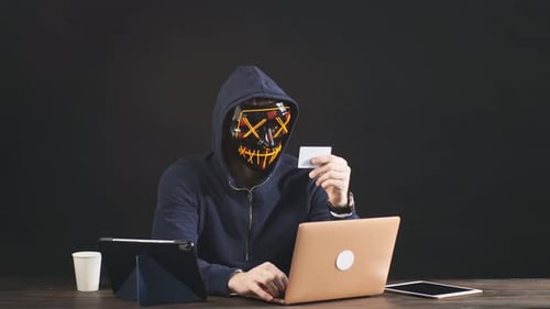 Hacker with Mask Using Laptop and Credit Card