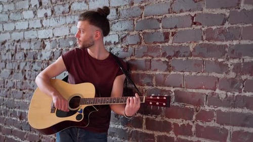 Man Playing Acoustic Guitar Against Brick Wall
