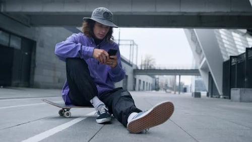 Young Adult Uses Phone on Skateboard in City