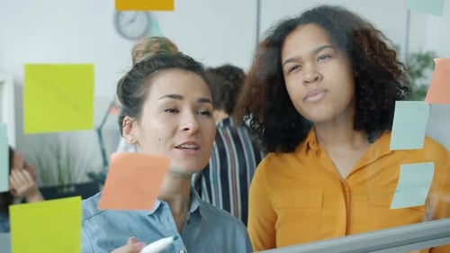 Collaborative Team Brainstorming on Glass Wall in Office