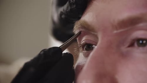 An Eyebrow Master Plucking the Hairs of the Eyebrow of His Male Client