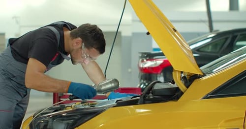 Man Repairing Yellow Car Engine in Auto Shop