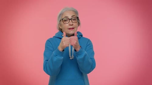 Ältere alte Frau zeigt mit verspieltem, fröhlichem Ausdruck auf die Kamera und zeigt die Richtung