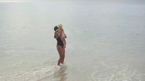 Mom with a Two-year-old Daughter Walking Along the Sandy Beach