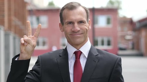 Smiling Man in Suit Holds Up Peace Sign