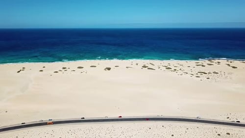 Above view of black asphalt road with desert and sand dunes around - coastline with blue ocean