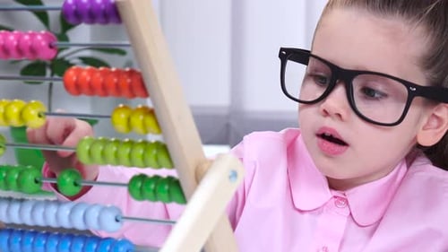 Una niña con gafas sentada a la mesa y le dijo a las cuentas multicolores. De cerca