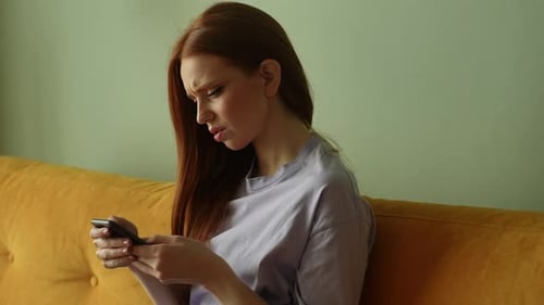 Woman Using Phone Looking Confused Indoors on Couch
