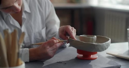 Woman Sculpting Pottery with Tool in the Studio