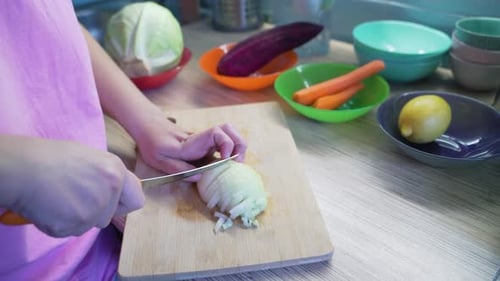Hands Slicing Onion in Kitchen with Vegetables
