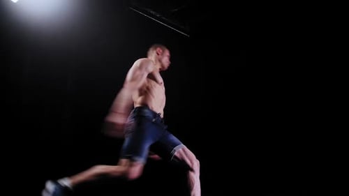 Shirtless Man Performing Gymnastic Moves in Dark Studio
