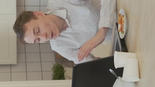 Tired Man Works at Laptop in Kitchen