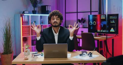 Businessman Sitting at the Table in Evening Office with Folded in Mudra Hands Gesture