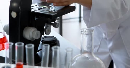 Schoolgirl experimenting on microscope in laboratory