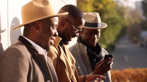 Three Friends Laughing and Using Cell Phones Outside
