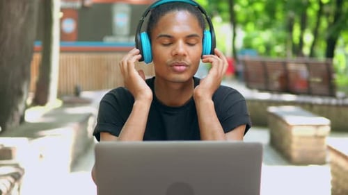 Young Adult Using Laptop and Headphones Outdoors