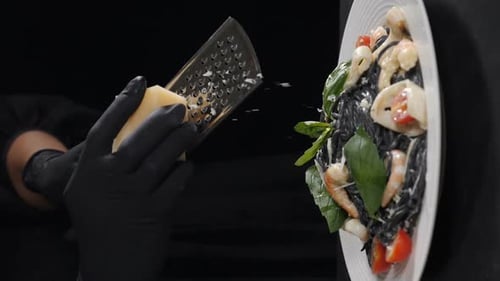 Koch reibt Hartkäse auf frisch gekochten schwarzen Meeresfrüchte-Nudeln