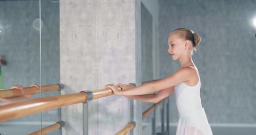 Smiling Girl with Bun Stands at Barre in Dance Studio