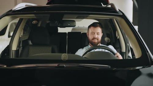 Man Sitting in Car in Showroom Inspecting Visor