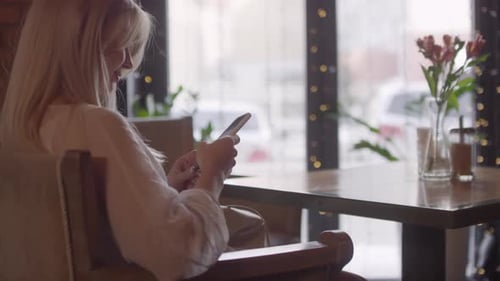 Blond Woman Sitting in Cafe and Using Mobile Phone