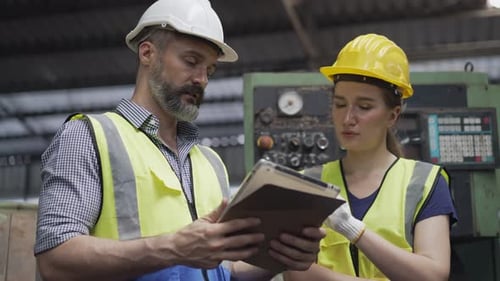 Man and Woman Inspecting Factory Equipment Using Tablet