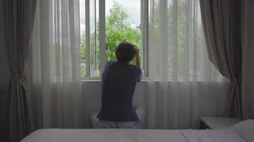 Ein junger Mann in einer obligatorischen Quarantäne. Er sitzt und schaut aus dem Fenster. Er bleibt in einem Zimmer