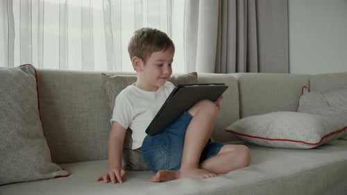 Little Boy Enjoys Tablet on Cozy Sofa