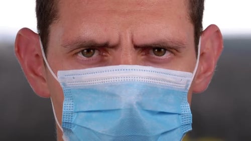 Young Man in a Medical Protective Face Mask Looking at the Camera on the Street Background