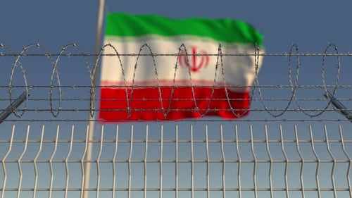 Blurred Waving Flag of Iran Behind Barbed Wire Fence