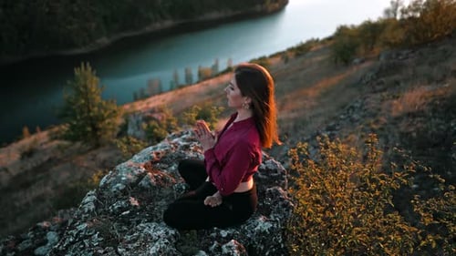 Concentrated Woman in Lotus Pose Doing Meditation on High Rock Above Water
