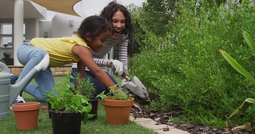 Hispanic mother and daughter teaching planting flowers in the garden