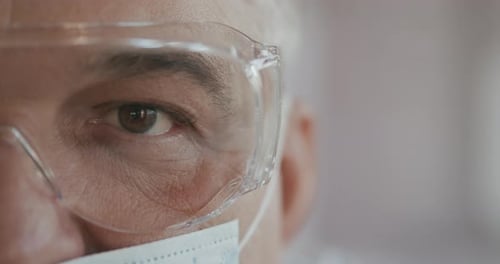 Male Doctor or Nurse in Uniform, Mask and Glasses Looking Straight at Camera. Close Up of Eye. Slow
